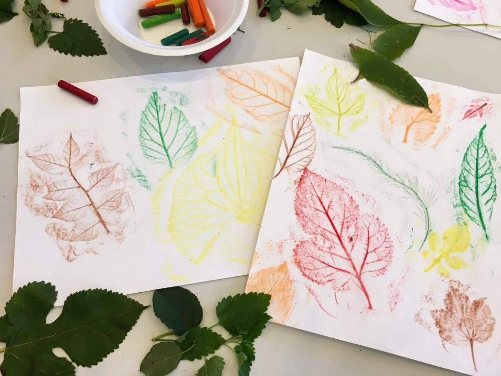 Crayons and leaves scattered around two pages with leaf textures colored on them.